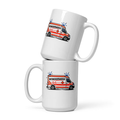 Lustige weiße Tasse mit Comic-Rettungswagen und dem Spruch „Nutzniesserfahrzeug“ in schwarzer und roter Schrift.